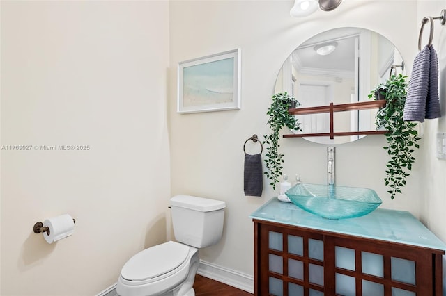 bathroom featuring wood finished floors, toilet, vanity, crown molding, and baseboards