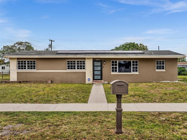 view of front of home with stucco siding, solar panels, and a front lawn