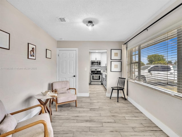 living area featuring light wood-style floors, a textured ceiling, baseboards, and visible vents