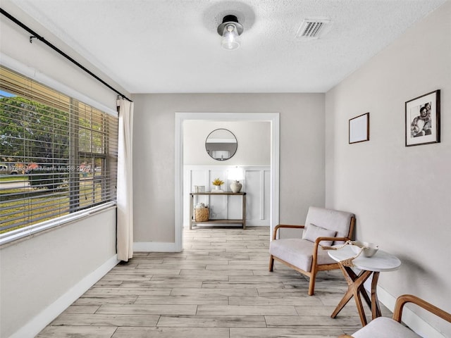 sitting room featuring light wood finished floors, baseboards, visible vents, and a textured ceiling