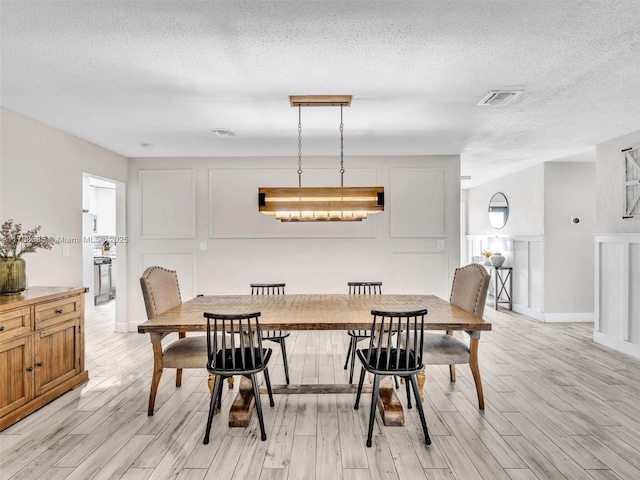 dining area with light wood-style flooring, visible vents, and a textured ceiling