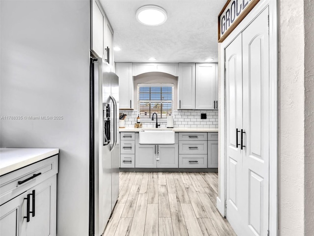 kitchen with a sink, light wood-type flooring, decorative backsplash, gray cabinets, and stainless steel fridge with ice dispenser