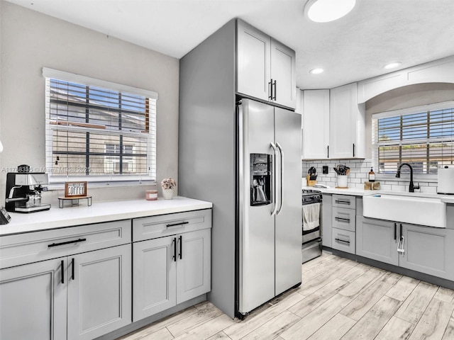 kitchen with light countertops, a sink, gray cabinetry, light wood-style flooring, and appliances with stainless steel finishes