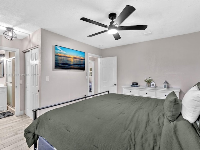 bedroom featuring ensuite bath, a textured ceiling, light wood-style floors, and ceiling fan