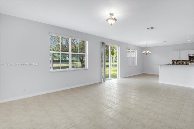 unfurnished living room featuring a chandelier, baseboards, visible vents, and a wealth of natural light