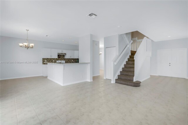 unfurnished living room with a chandelier, baseboards, visible vents, and stairs
