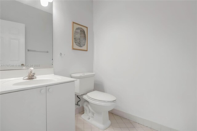 half bath with tile patterned floors, baseboards, vanity, and toilet