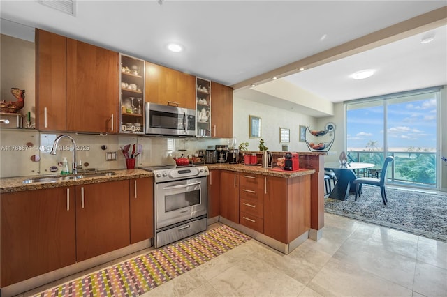 1945 S Ocean Dr Unit 401, Hallandale Beach, FL 33009 - kitchen featuring stainless steel appliances, brown cabinets, a peninsula, decorative backsplash, and stone counters