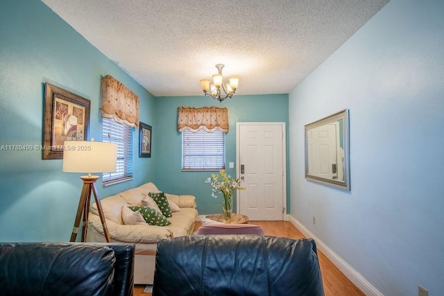 living area with baseboards, wood finished floors, a textured ceiling, and a notable chandelier