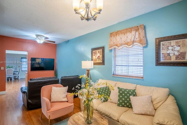 living area with ceiling fan with notable chandelier, wood finished floors, and a textured ceiling