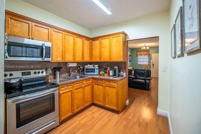 kitchen featuring brown cabinets, stainless steel appliances, backsplash, a sink, and light wood-style floors