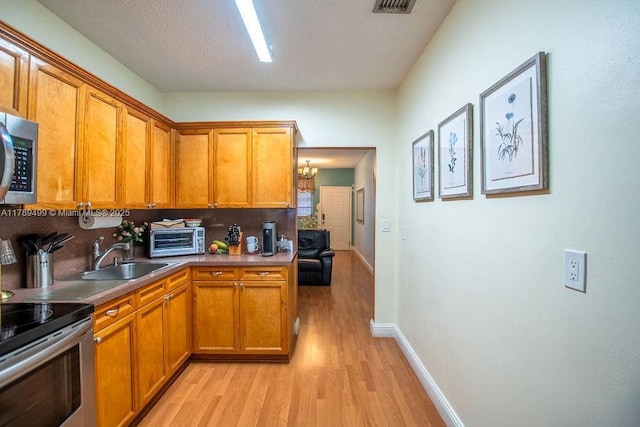 kitchen featuring a sink, brown cabinetry, decorative backsplash, light wood-style floors, and stainless steel appliances