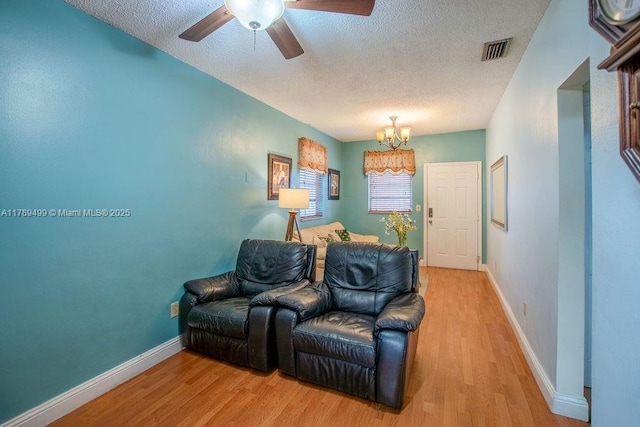 living area with a textured ceiling, ceiling fan with notable chandelier, light wood-style flooring, baseboards, and visible vents
