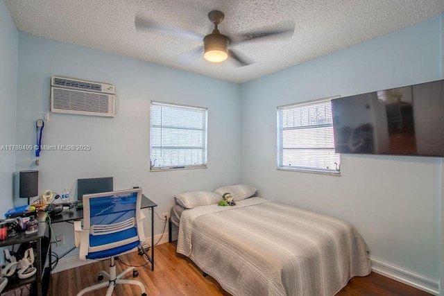 bedroom featuring a wall mounted AC, wood finished floors, a textured ceiling, and a ceiling fan