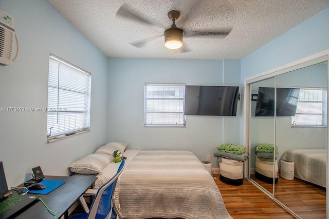 bedroom with wood finished floors, multiple windows, a textured ceiling, and a closet