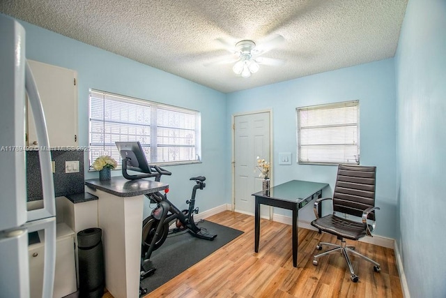 home office with light wood-type flooring, a textured ceiling, a ceiling fan, and baseboards