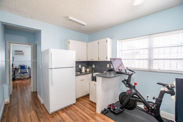 kitchen featuring white cabinets, dark countertops, freestanding refrigerator, light wood-style floors, and a wall mounted AC