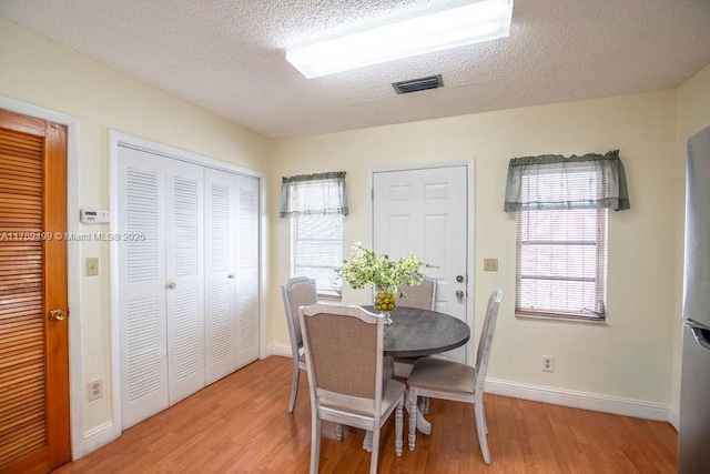 dining room featuring baseboards, a textured ceiling, visible vents, and light wood-type flooring