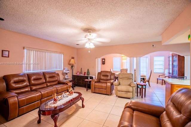 living area with ceiling fan, arched walkways, a textured ceiling, and light tile patterned floors