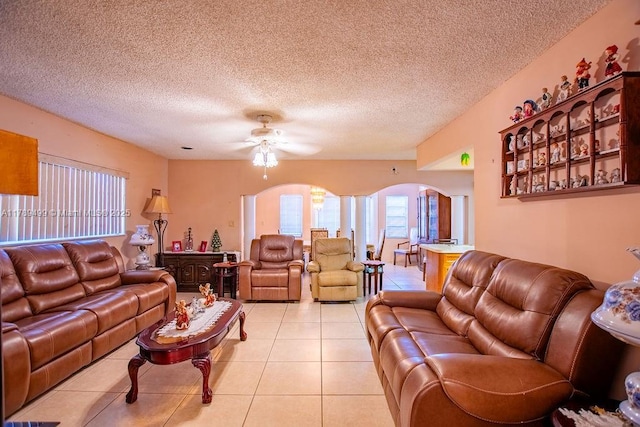 living room featuring arched walkways, a textured ceiling, ceiling fan, and light tile patterned floors