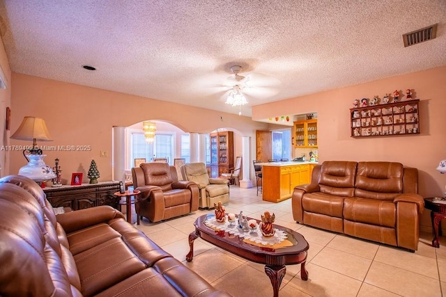 living area with arched walkways, a textured ceiling, light tile patterned flooring, visible vents, and ceiling fan