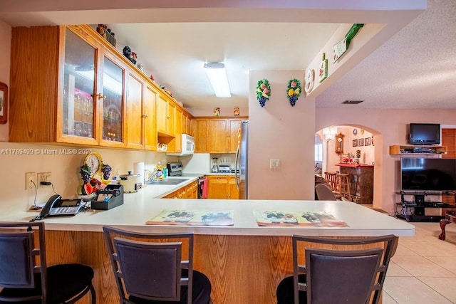 kitchen with a peninsula, light countertops, arched walkways, and appliances with stainless steel finishes