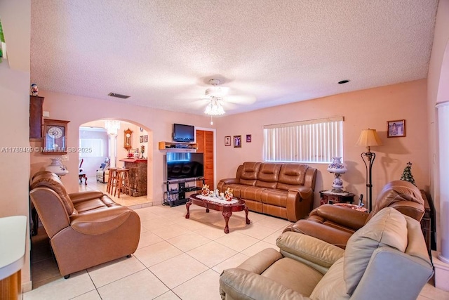 living room with a ceiling fan, a textured ceiling, light tile patterned floors, arched walkways, and visible vents