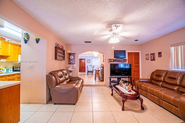 living area featuring a textured ceiling, light tile patterned floors, ceiling fan, arched walkways, and visible vents