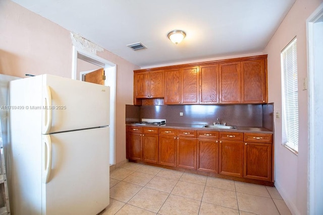 kitchen with a sink, tasteful backsplash, visible vents, freestanding refrigerator, and brown cabinets