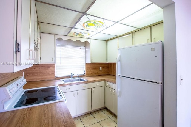 kitchen featuring a drop ceiling, light countertops, light tile patterned floors, a sink, and white appliances