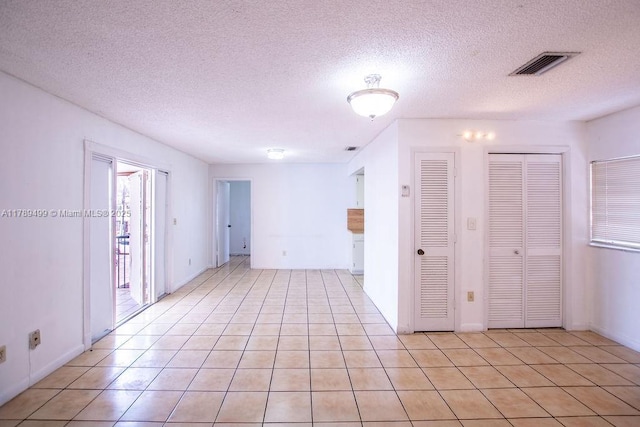 spare room with a textured ceiling, visible vents, baseboards, and light tile patterned floors
