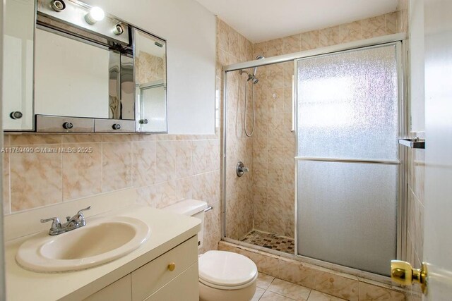 bathroom featuring a shower stall, tile patterned floors, toilet, vanity, and tile walls
