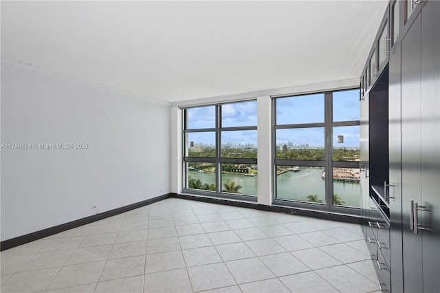 spare room featuring light tile patterned floors, a water view, a city view, baseboards, and ornamental molding
