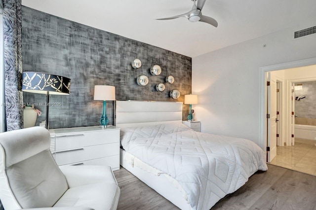 bedroom with an accent wall, a ceiling fan, wood finished floors, and visible vents