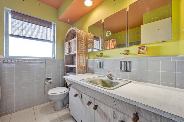 full bath with tile patterned flooring, toilet, vanity, tile walls, and wainscoting