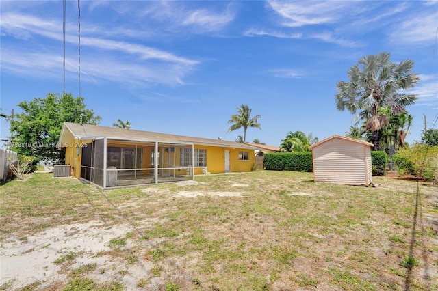 rear view of house featuring an outdoor structure, a lawn, a storage unit, and a sunroom
