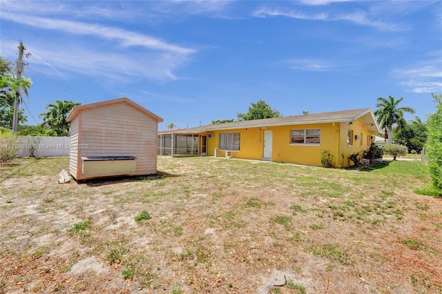 back of property featuring fence, an outdoor structure, a lawn, a storage unit, and a sunroom