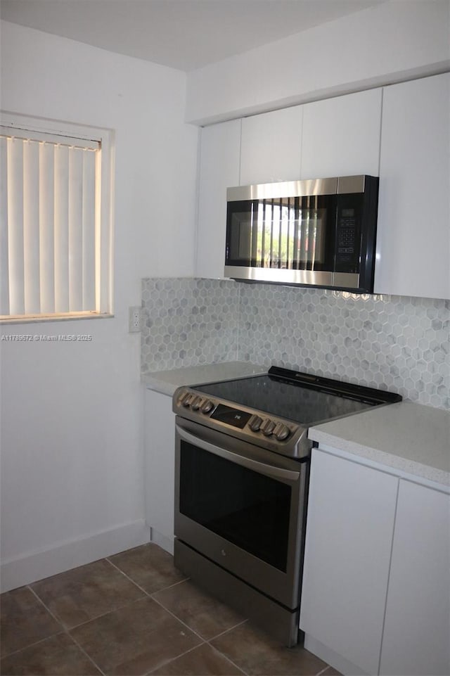 3490 Foxcroft Rd Unit B304, Miramar, FL 33025 - kitchen with appliances with stainless steel finishes, decorative backsplash, white cabinetry, dark tile patterned flooring, and light countertops