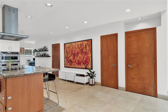 3730 Kumquat Ave, Miami, FL 33133 - kitchen with dark stone counters, island range hood, light tile patterned flooring, a breakfast bar, and recessed lighting