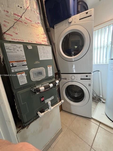 laundry area with tile patterned floors, heating unit, stacked washing maching and dryer, and laundry area