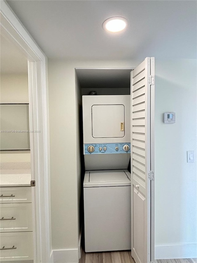 laundry area with stacked washer / drying machine, wood finished floors, baseboards, and laundry area