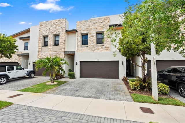 view of front of property with stucco siding, an attached garage, decorative driveway, and stone siding