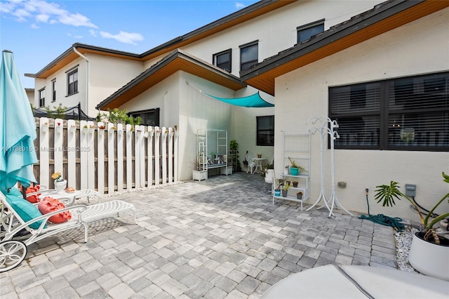 rear view of house featuring stucco siding, fence, and a patio area