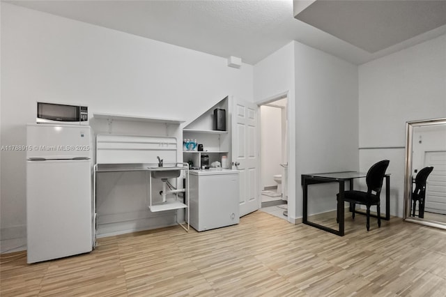kitchen featuring open shelves, white microwave, light wood-style floors, and fridge