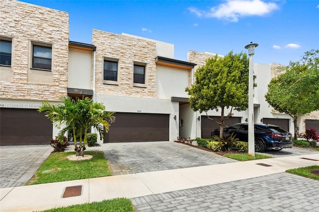 contemporary house with stucco siding, an attached garage, stone siding, and decorative driveway
