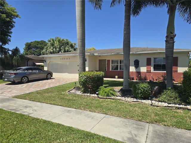 ranch-style home with a front lawn, brick siding, an attached garage, stucco siding, and decorative driveway