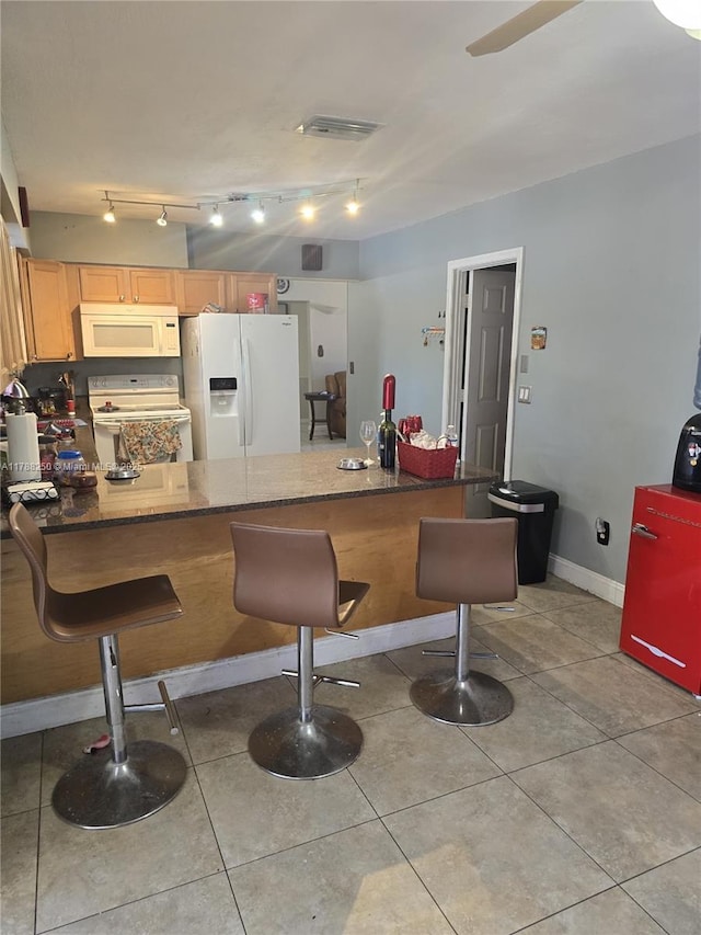 kitchen featuring visible vents, white appliances, light tile patterned flooring, a peninsula, and a kitchen bar