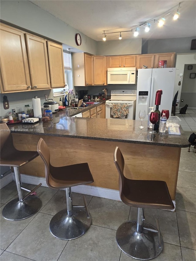 kitchen featuring a kitchen breakfast bar, dark stone countertops, tile patterned floors, white appliances, and a peninsula