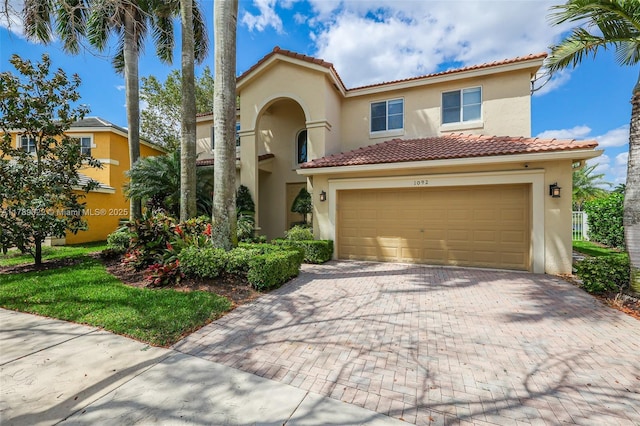 mediterranean / spanish home featuring a garage, a tile roof, stucco siding, and decorative driveway