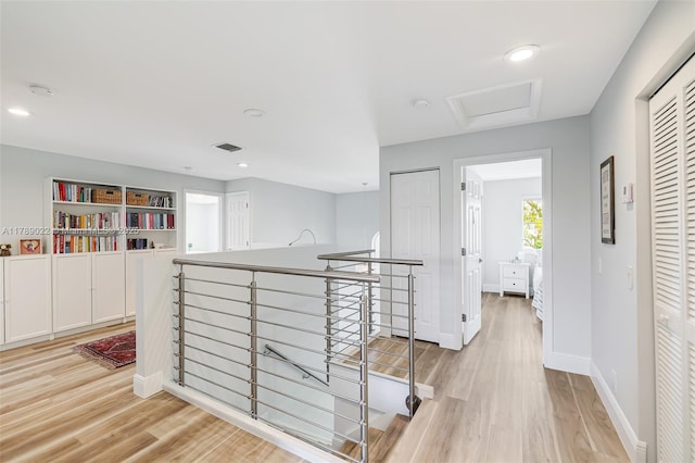 corridor with an upstairs landing, light wood-type flooring, baseboards, visible vents, and recessed lighting